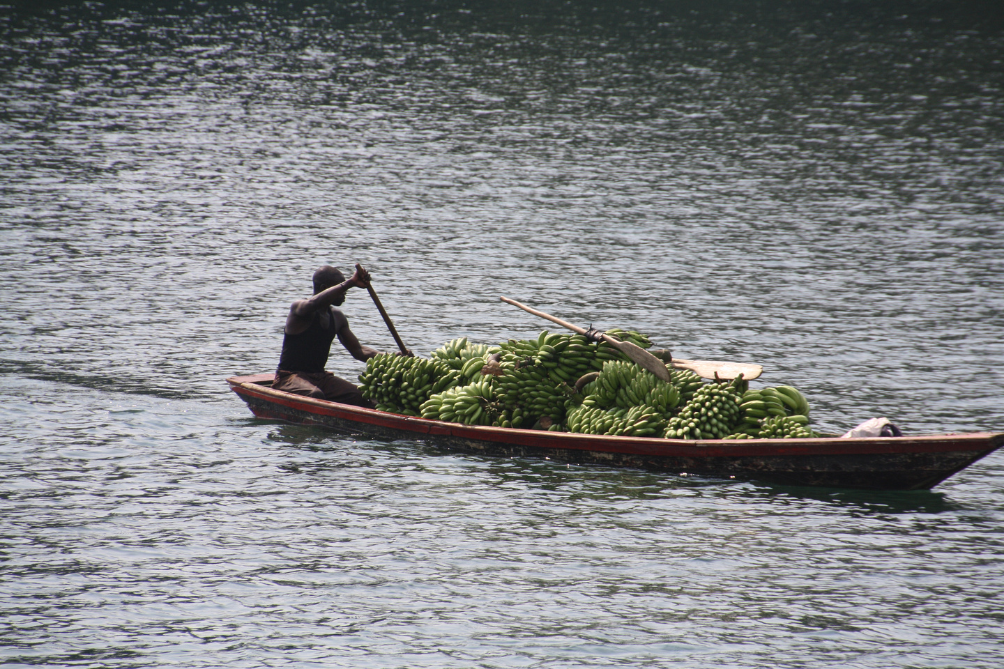 Inwoner van Rwanda vervoert bananen met een boot door af te zetten met een lange stok.
