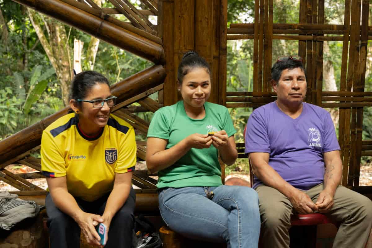 Drie mensen zitten in de gemeenschapsruimte van Sinchi Warmi, betrokken bij lokale activiteiten.