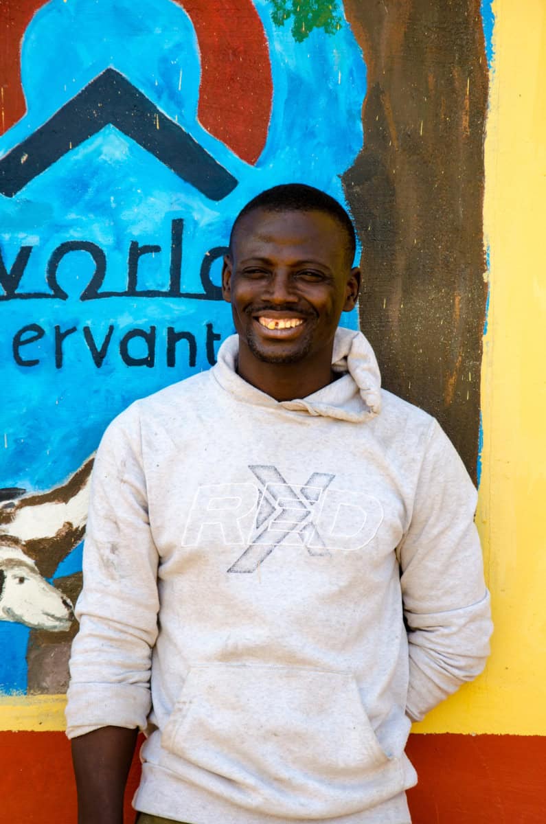 Vrijwilliger van Wereldservants glimlacht voor kleurrijke muur.